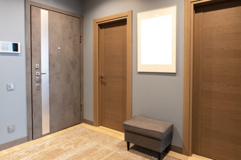 Modern entrance hallway in neutral shades of brown and gray tones. On wall there is photo frame with mockup, front door with intercom. Concept fashionable interior design, use of natural materials.